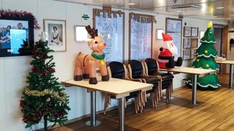 BAS Decorations including Christmas trees and an inflatable reindeer and Santa are seen in part of a chip. There is a Merry Christmas banner on the wall, which is adorned with photographs including one of Queen Elizabeth II