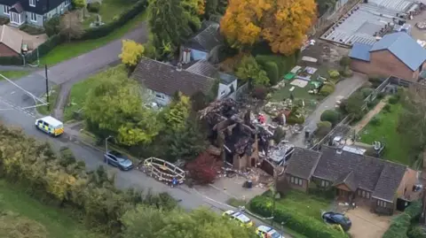 Ant Saddington/BBC Drone photo shows destroyed buildings with emergency vehicles parked outside. Nearby homes appear undamaged.