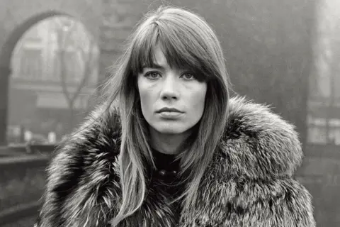 Getty Images Françoise Hardy photographed in the 1960s on what looks like a winter's day in Paris. She has long brown hair and wears a thick fur coat. She stares directly and seriously at the camera