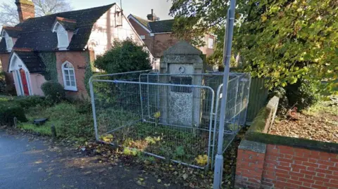 Google The war memorial in Shrub End in Colchester, prior to its restoration, surrounded by metal fencing