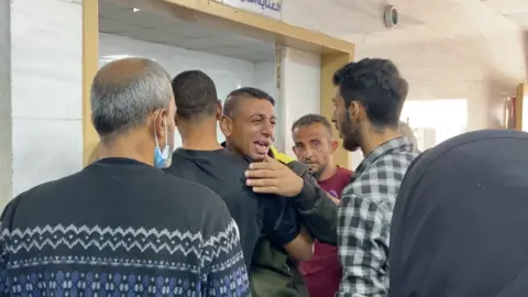 An emotional man is comforted by other men at the Kamal Adwan Hospital