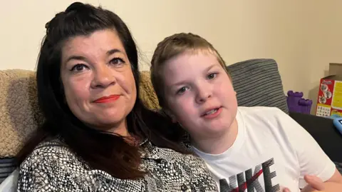 BBC A dark haired lady with her young son in a white t-shirt sitting in their living room