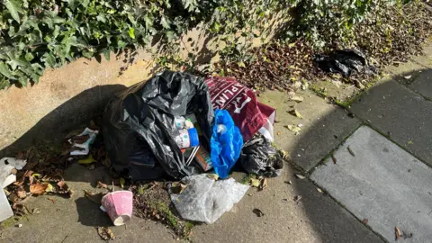 BBC Black bin split open on the street with rubbish coming out of it