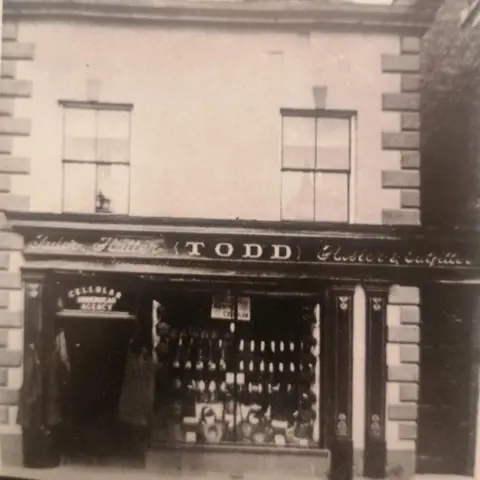Public domain A grainy, black and white photograph of a haberdashery shop front showing the word Todd above the window.
