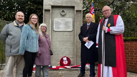John Fairhall/BBC The family of Kevin Starling stand next to the war memorial in Shrub End, along with Sir Bob Russell, High Steward of Colchester, and the Bishop of Colchester, the Right Reverend Roger Morris