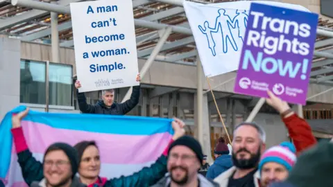 PA Media Gender law protests outside Holyrood. The crowd of men and women are holding pro and anti trans rights posters.