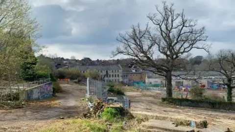 Mayday Saxonvale Abandoned site in Frome looking derelict, it has old fences, scrubs and houses in the background.