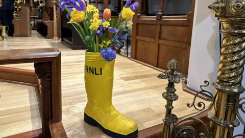 BBC A yellow wellington boot with RNLI written on it holding colourful flowers.