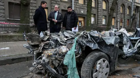 Getty Images The prime minister guided by Ukrainian officials as he inspects a damaged vehicle along a street