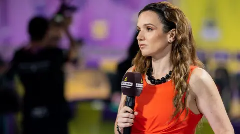 Michael Konkol Esports commentator, Sam Wright holding a microphone and wearing an orange dress