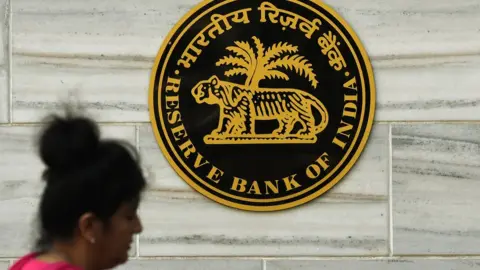 Getty Images An Indian woman walks past the logo of India's central bank, the Reserve Bank of India (RBI), in Mumbai on November 9, 2016.