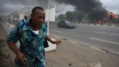Getty Images People walk past a fire service station set ablaze by members of the Shia Islamic Movement in Nigeria (IMN) during clashes with the police in the streets of Abuja on July 22, 2019.