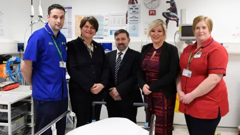 Michael Cooper Arlene Foster, Robin Swann and Michelle O'Neill pictured alongside health workers