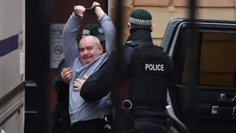 Getty Images Paul McIntyre, the man charged with the murder of Lyra McKee, raises his arms as he arrives at Londonderry Magistrates' Court on 13 February 2020 in Londonderry, Northern Ireland