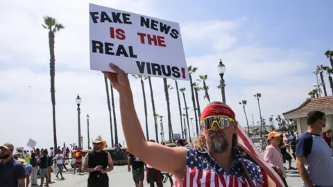 Getty Images A man holds a sign during a demonstration in California in early May saying "Fake news is the real virus"