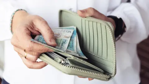 Getty Images A woman opening her purse and looking at money