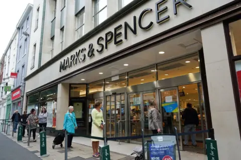 Getty Images Women stand in a socially distanced queue outside an M&S store