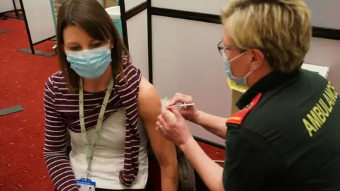 PA Media A woman receives her Covid-19 vaccine along with other health and social care workers at a mass vaccination centre in Newcastle