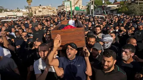 Getty Images Arab Israelis gesture and wave Palestinian flags during a funeral in the central Israeli city of Lod near Tel Aviv