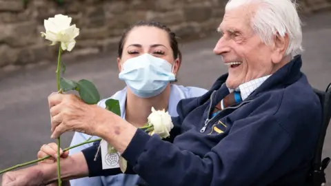 PA Media Health Care Assistant Rose Waddington and ninety-eight-year-old resident John Kykot are pictured with "thank you" white roses that were presented to them by the Mayor of West Yorkshire Tracy Brabin at Norwood House Nursing Home in Keighley, as part of the first-ever national Thank You Day