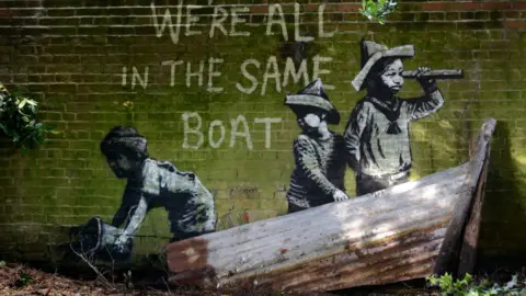 PA Media Banksy artwork in Oulton Broad, Suffolk, shows a group of children playing in a makeshift boat - painted on a drain bridge