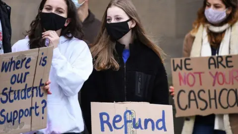 Getty Images Three students at a protest, holding up signs saying 'Where is our student support?' and 'Refund'