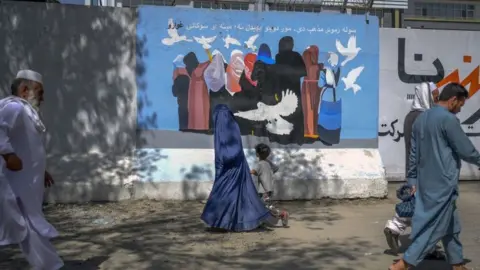 Getty Images A burqa-clad woman along with a boy walks past a mural depicting women and doves flying along a street in Kabul on September 15, 2021