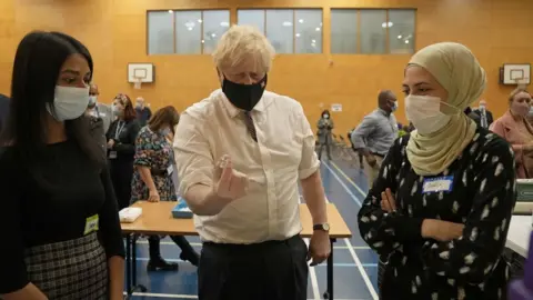 PA Media Boris Johnson holding a dose of the Pfizer vaccine next to two women