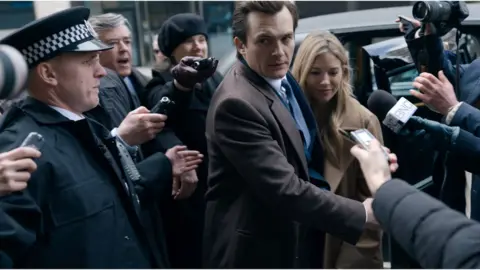 Netflix Policeman and press photographers surrounding a man and woman