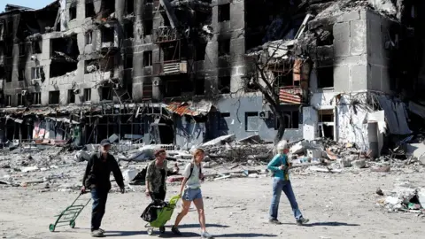 Reuters Local residents walk past an apartment building destroyed during Ukraine-Russia conflict in the southern port city of Mariupol