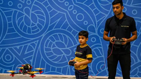 Getty Images A boy learns to fly a drone under the supervision of a professional drone operator at the "Bharat Drone Mahotsav 2022" drone show in New Delhi on May 27, 2022.