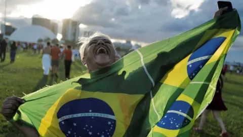 Reuters A supporter of Brazil's President Luiz Inacio Lula da Silva reacts holding a flag after gathering to listen to his speech at the Planalto Palace, in Brasilia, Brazil, January 1, 2023