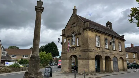 BBC a cream stone building next to a tall stone pillar and a cloudy sky