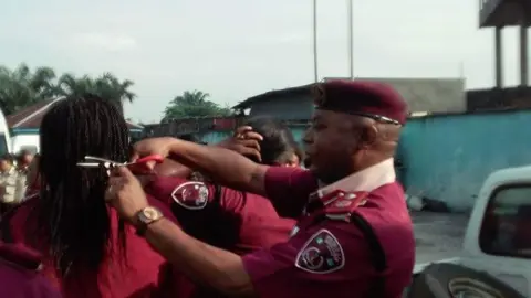 FRSC Rivers State/Facebook Man in maroon beret cuts a woman's hair in public