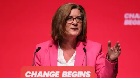 EPA Eluned Morgan stood at a lectern at a Labour conference with the words "change begins" in capital letters written on a screen behind her and on the lectern.