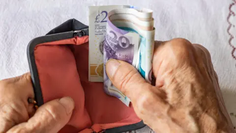 Getty Images A pensioner's hands counting bank notes over an old-fashioned purse.