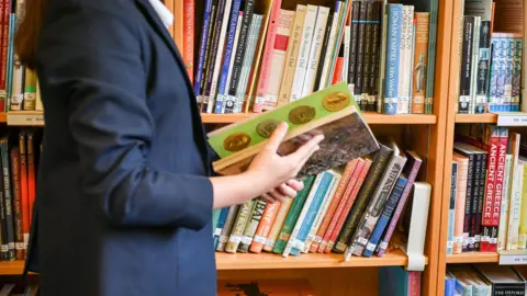 PA Media Woman walking past library shelf while flicking through book