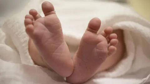 Getty Images Image of a newborn baby's feet. All toes are visible. The baby is wrapped in a white blanket