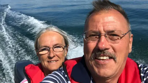 Paul Ainsworth Janet and Paul Ainsworth on a boat, with water in the background. They are both wearing glasses and red life jackets. 