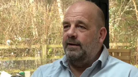 BBC A picture of Andy Smith sitting down inside, behind a garden.