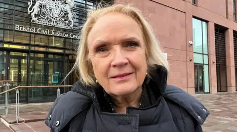 BBC Beverley Watkins, managing partner of Watkins Solicitors in Bristol. She has blonde hair and is wearing a grey coat, standing outside the Bristol Civil Justice Centre.