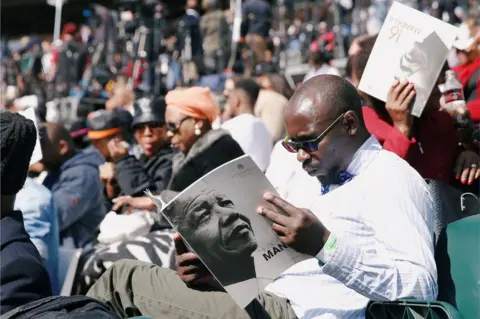 AFP A man holds a program as crowds gather to hear former U.S. President Barack Obama delivering the 16th Nelson Mandela annual lecture, marking the centenary of the anti-apartheid leader's birth, in Johannesburg, South Africa July 17, 2018.