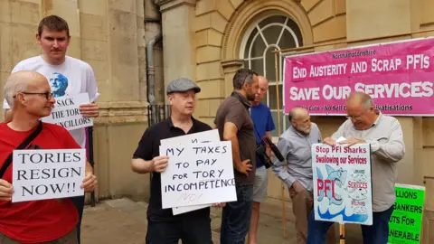 About 20 people gathered outside County Hall to protest against cuts.