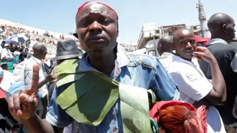 Reuters A Kenyan carrying a cock reacts as he attends a memorial service for late former Kenya's President Daniel arap Moi at the Nyayo Stadium in Nairobi, Kenya February 11, 2020.