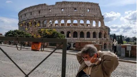 EPA A tourist wearing a mask sits at the tables of a restaurant in front of the Colosseum, in Rome, Italy, 9 March 2020.