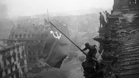 Getty Images A Soviet soldier pictured hoisting a flag over the Reichstag in 1945