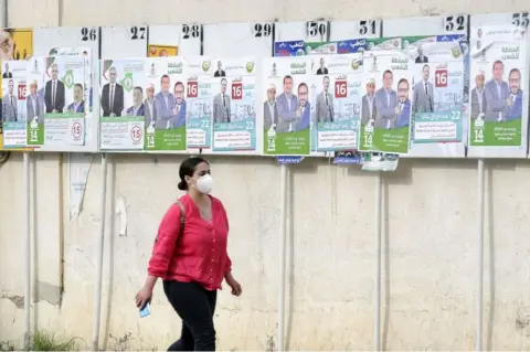 Getty Images A woman walks past the political adverts in Algers, Algeria, on 8 June.