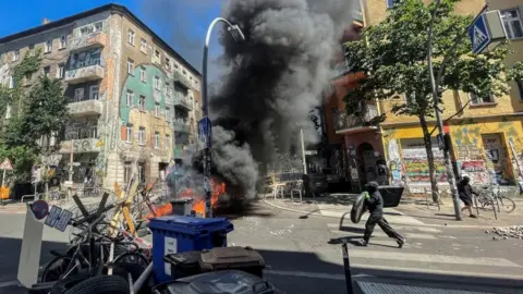 Reuters A man holding an object runs toward burning barricades at Rigaer Street in Berlin