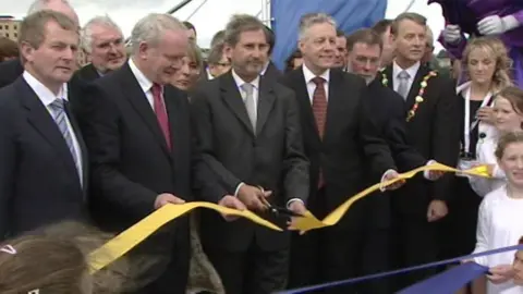 Enda Kenny, Martin McGuinness, Peter Robinson and other politicians watch as Johannes Hahn cuts the ribbon to officially open the Peace Bridge