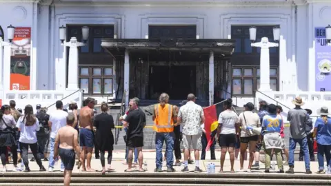 EPA People stand in front of the burned out entrance doors to Old Parliament House in Canberra, Australia, 30 December 2021